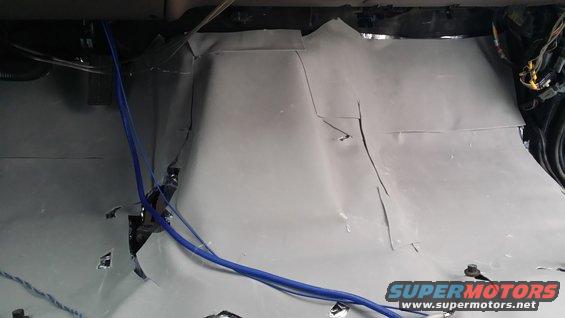 Interior of a vehicle with gray soundproofing material and blue wires visible