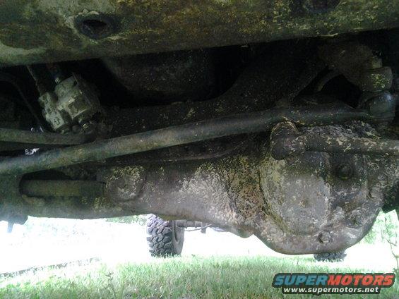 Undercarriage of a dirty vehicle, showing suspension and differential. A tire is visible on the right