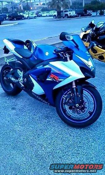 Blue and white Suzuki sport motorcycle parked on asphalt, another yellow motorcycle visible behind it