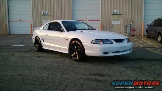 White 1996 Ford Mustang GT coupe with black wheels parked in front of a garage