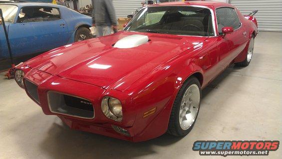 Red 1970s Pontiac Firebird with shaker hood scoop and aftermarket wheels