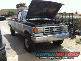 Silver and black Ford F-Series truck with hood open, showing engine. Chrome grille and bumper
