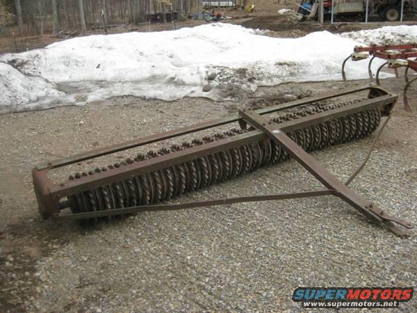 Agricultural roller with metal discs on a gravel surface with snow in the background