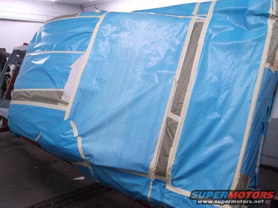 Car body covered in blue plastic sheeting and taped for painting