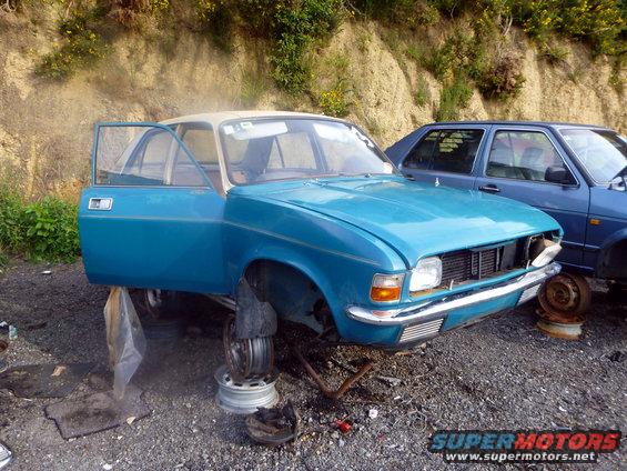 blue sedan on blocks, doors open, missing wheels, next to a blue hatchback