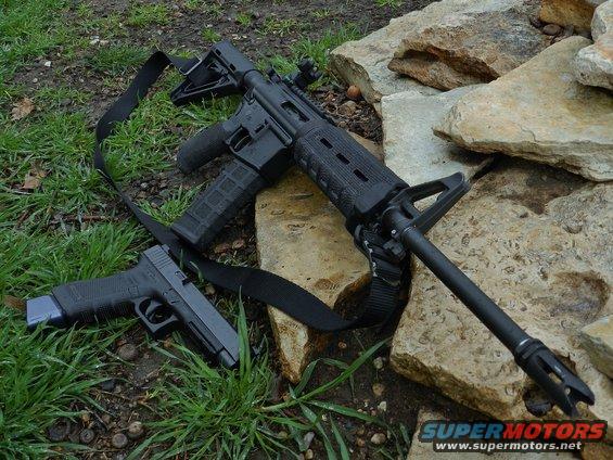 Assault rifle and handgun on grass and rocks. Supermotors.net logo visible