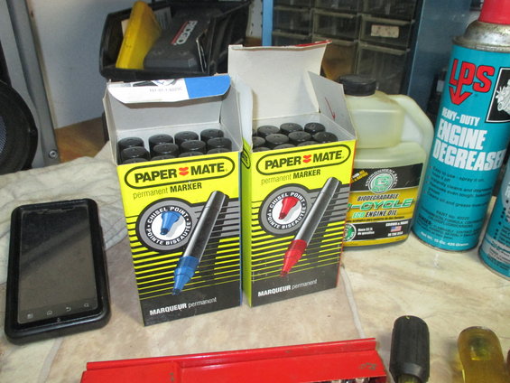 Two boxes of Paper Mate permanent markers, a black smartphone, and bottles of engine degreaser and oil on a counter
