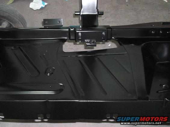 Black metal car frame section with stamped diagonal lines and mounting brackets. A tire is partially visible on the left