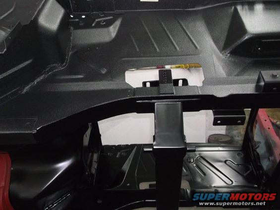 Black interior floor pan with visible structural supports and a tool on a white bracket