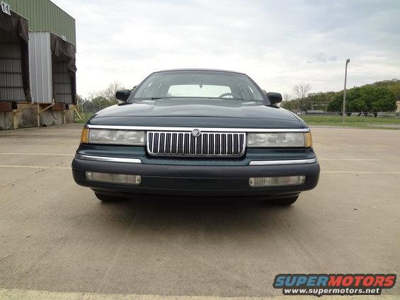 Dark green sedan front view, chrome grille, black bumper, cloudy sky