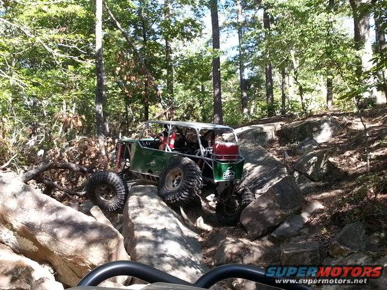 Green off-road buggy with large tires navigating a rocky trail in a forest