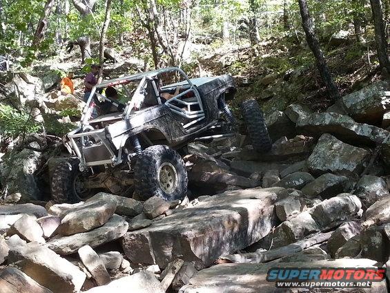 Modified off-road buggy with roll cage climbing over large rocks on a wooded trail