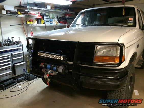White Ford Bronco front view with black bull bar, winch, and LED light bar. Garage setting