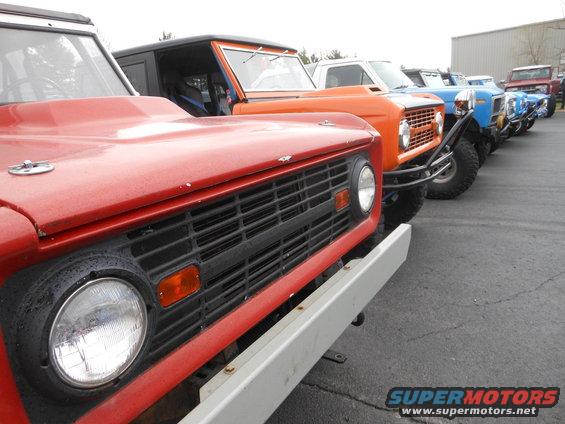 Red 1978 Ford Bronco front end, bumper, and grille, parked in a line with other Broncos