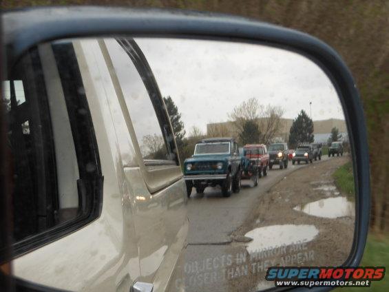 Line of Ford Broncos driving down a dirt road, seen in a side mirror