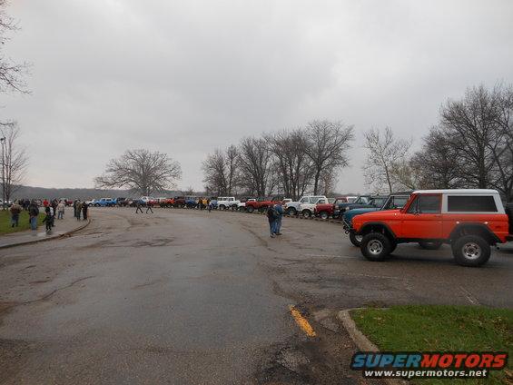 Orange first-generation Bronco with white top, parked in a lot with many other vehicles