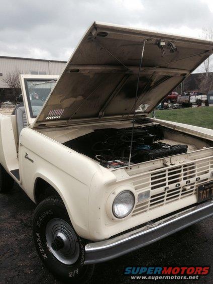 Cream-colored first-generation Ford Bronco with hood open, showing engine and grille