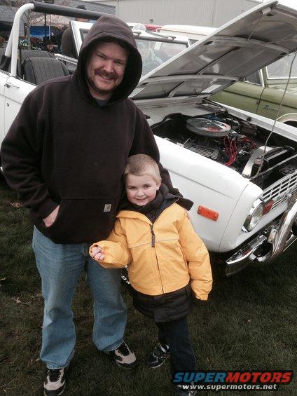 Man and child stand in front of a white Ford Bronco with hood open. Another vehicle is partially visible behind it