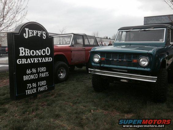 Teal 1969 Ford Bronco front end, red Ford Bronco behind it, and a sign for Jeff's Bronco Graveyard