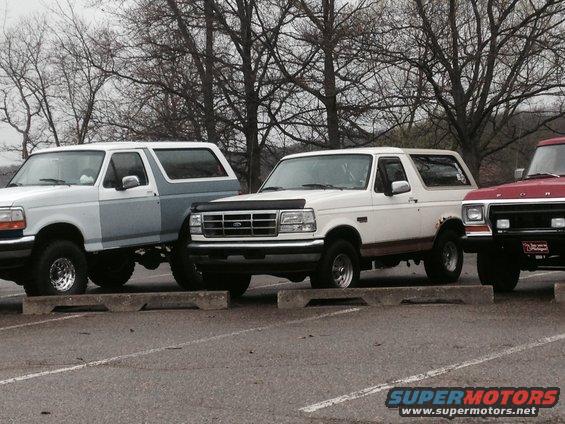 White 1995 Ford Bronco parked next to another Bronco and a red truck