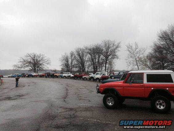 Line of Ford Broncos parked by a lake, one red Bronco in foreground