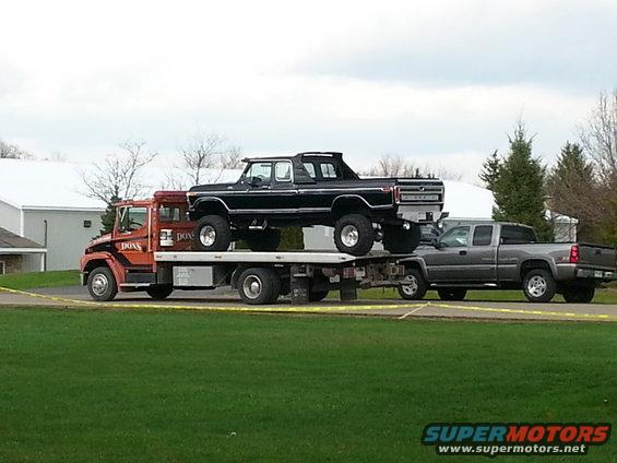 Black lifted pickup truck with a camper shell on a flatbed tow truck, side view