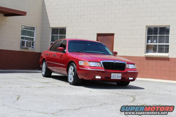 Red 2002 Mercury Grand Marquis parked in front of a brick building, license plate reads EVIL MGM