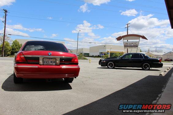 Red sedan from rear, black sedan parked nearby. License plate says EVIL MGM