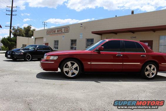 Red 2002 Mercury Grand Marquis parked next to a black police-style sedan outside a building
