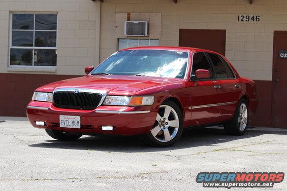 Red 2002 Mercury Grand Marquis parked in front of a building. License plate says EVIL MGM