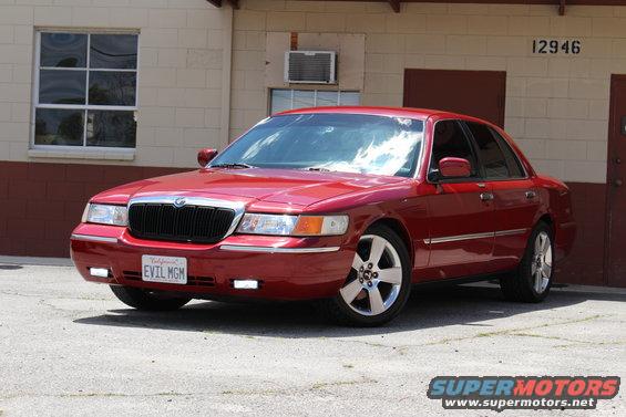 Red 2002 Mercury Grand Marquis parked outside a building. License plate says EVIL MGM