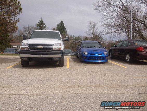 White pickup truck parked next to a blue Dodge Neon SRT-4. Another car is parked to the right