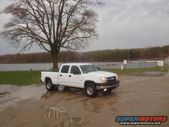 White 2006 Chevrolet Silverado 2500 parked on wet ground near a lake
