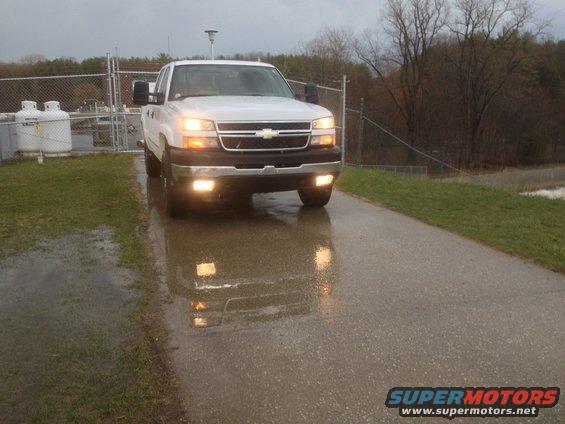 White pickup truck with headlights on, parked on a wet road