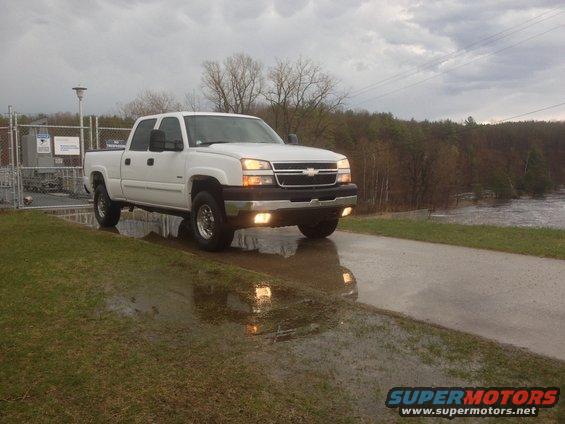 White pickup truck parked on wet asphalt, front 3/4 view. Grille and headlights visible