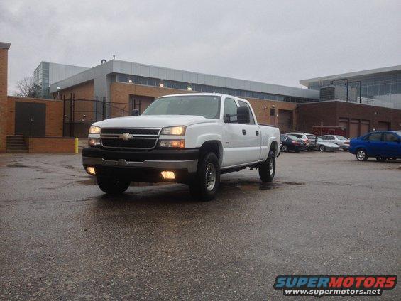 White 2006 Chevrolet Silverado 2500 parked on wet asphalt in front of a brick and glass building