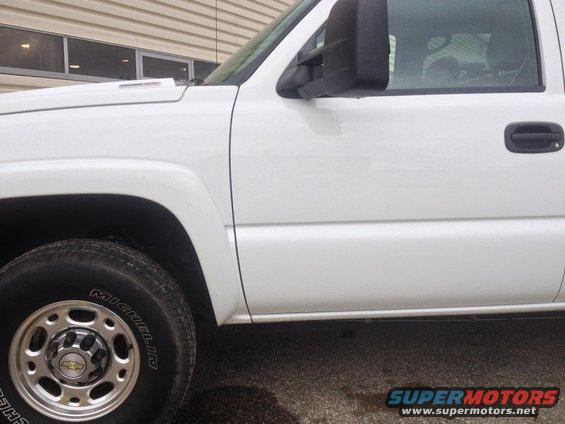 Side view of a white Chevrolet Silverado pickup truck, showing the front fender, door, and wheel