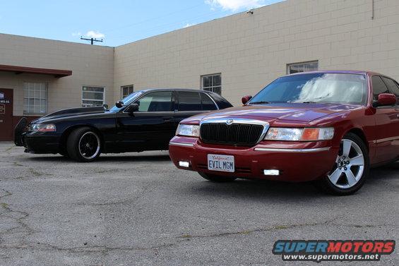 Red 2002 Mercury Grand Marquis front 3/4 view, black sedan behind it