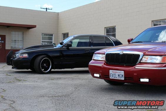 Red Mercury Grand Marquis with custom grille and black hood, parked next to a black Mercury Grand Marquis with a modified hood