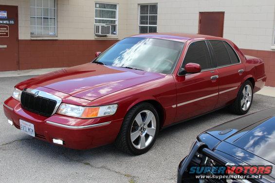 Red 2002 Mercury Grand Marquis with chrome trim and tinted windows parked next to a black vehicle