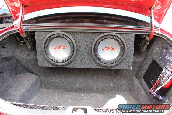 Car trunk with two subwoofers and an amplifier. A red car's trunk lid is open