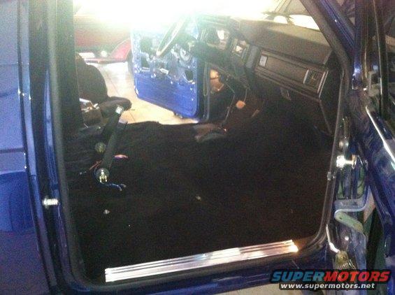 Interior view of a blue vehicle with door panels removed and carpet installed
