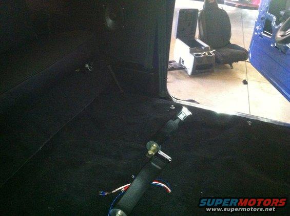Black carpeted interior of a vehicle with a seat and center console visible, and a seatbelt in the foreground
