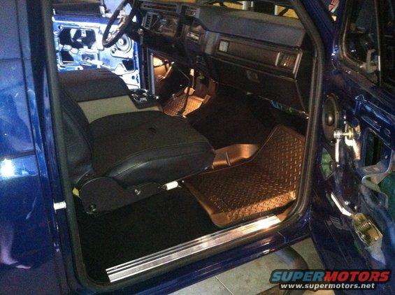 Interior view of a blue vehicle, showing seats, dashboard, and door panel. The door is open