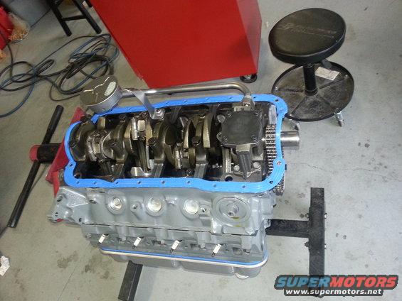Engine block with crankshaft, connecting rods, and oil pan gasket. A red tool chest and stool are in the background