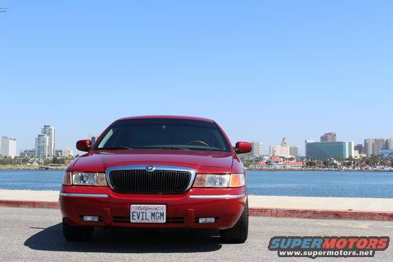 Red 2002 Mercury Grand Marquis parked by the water with a city skyline in the background. License plate reads EVIL MGM