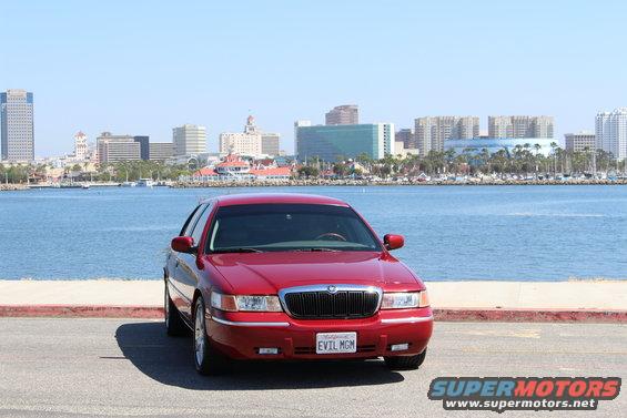 Red 2002 Mercury Grand Marquis parked by the water with city skyline in background