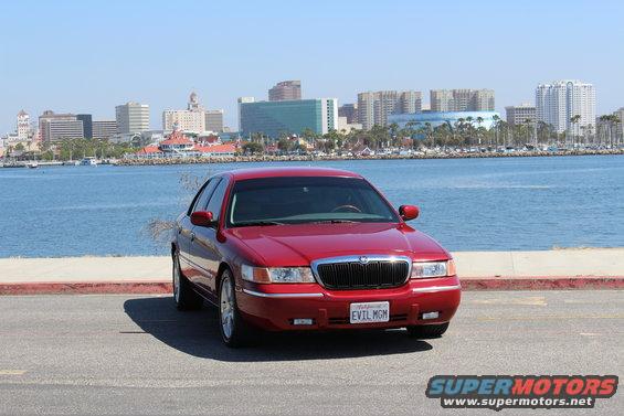 Red 2002 Mercury Grand Marquis parked by the water with a city skyline in the background