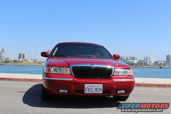Red 2002 Mercury Grand Marquis parked by the water with city skyline in background. License plate says EVIL MGM