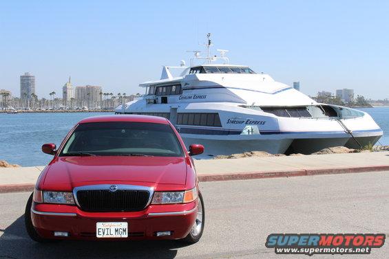Red 2002 Mercury Grand Marquis with a custom license plate "EVIL MGM" parked by a harbor